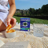 Person sitting outdoors with Visionace Plus eye supplement box, fruit, and glass of water on a blanket.
