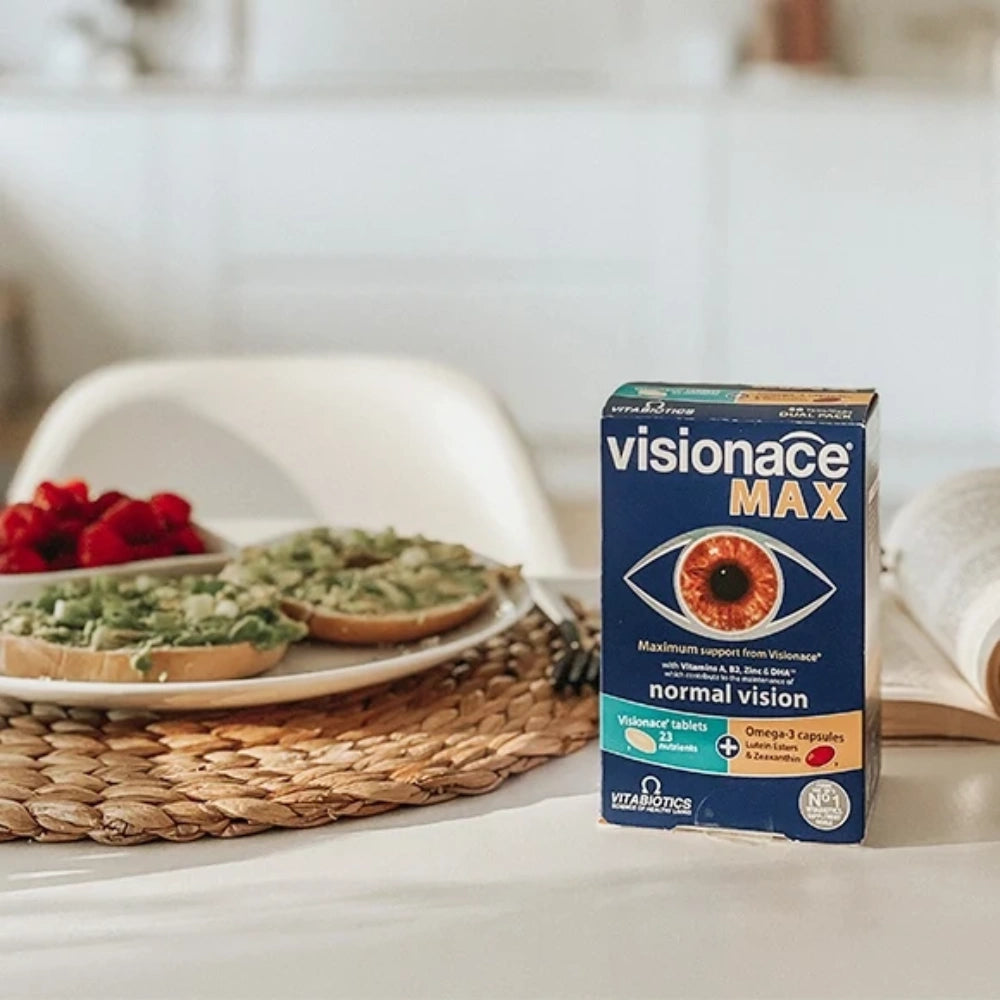 A box of visionace MAX eye drops for normal vision, placed on a white table next to a plate of avocado toast and berries in a bright, modern kitchen setting.