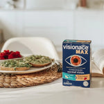 A box of visionace MAX eye drops for normal vision, placed on a white table next to a plate of avocado toast and berries in a bright, modern kitchen setting.
