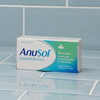 Box of Anusol suppositories on a reflective surface with tiled background