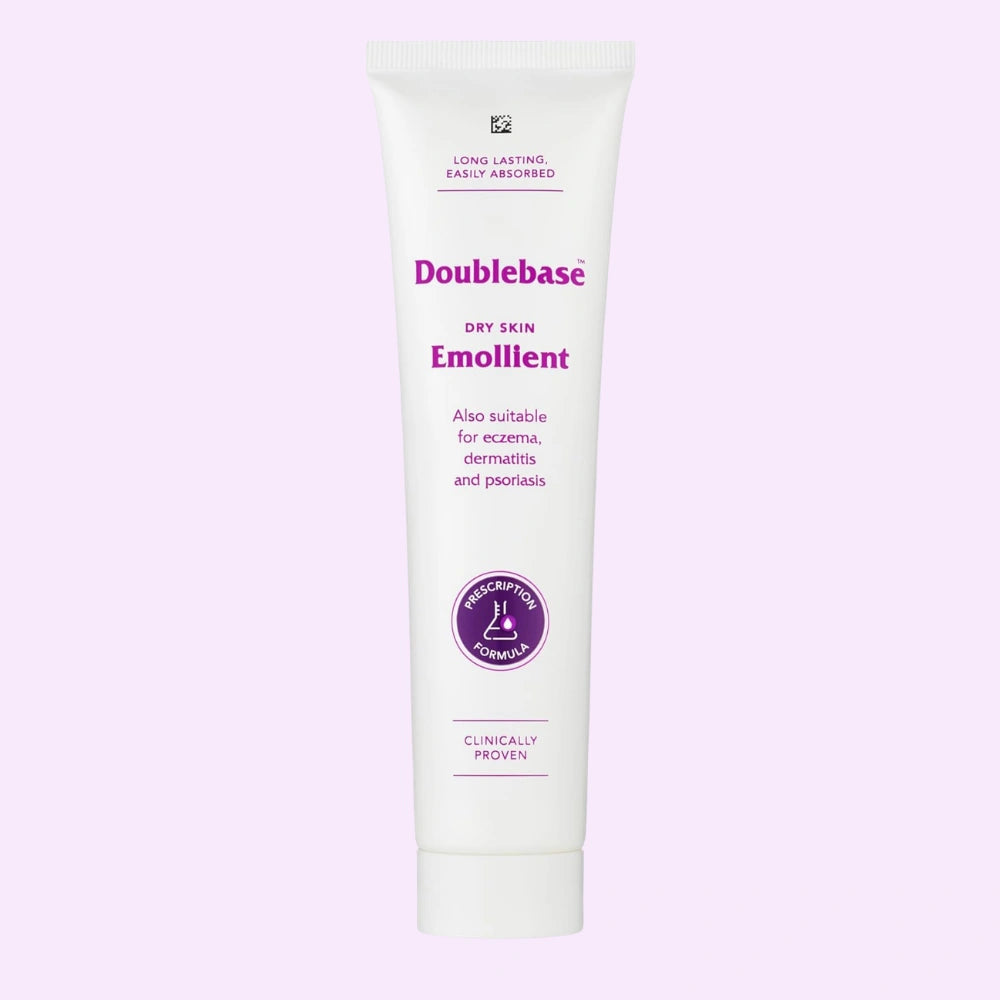 A white squeeze tube of Doublebase Dry Skin Emollient 100g with purple text and a purple circular seal, centered on a light lavender background.