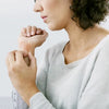 A close-up lifestyle shot of a woman in a light gray knit sweater holding and examining her wrist, shown from the side against a clean white background.