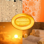 A collage-style product image centered on a round golden bar of soap embossed with 'PEARS TRANSPARENT SOAP.' Surrounding the soap are four warm-toned panels showing water droplets, orange soap foam, a glowing sunset, and spa towels, with '55ml' text in the lower left.