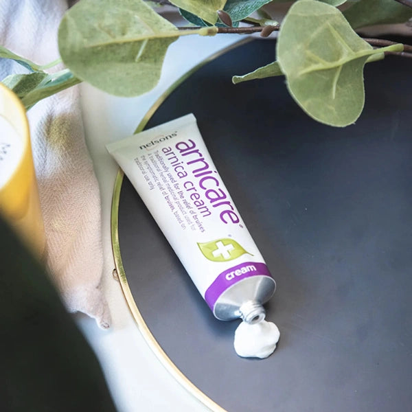 Tube of Arnica Cream on a dark surface with leaves in the background