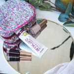 Cosmetic bag with lip gloss, nail polish, and a tube of cream on a mirror surface.