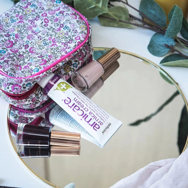 Cosmetic bag with lip gloss, nail polish, and a tube of cream on a mirror surface.