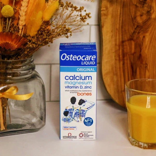 Osteocare Liquid supplement box placed beside orange juice and dried flowers on counter.