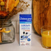 Osteocare Liquid supplement box placed beside orange juice and dried flowers on counter.