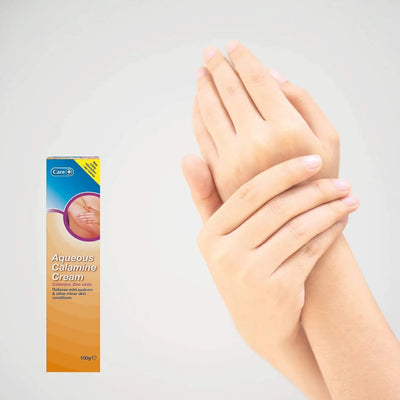 Box of Aqueous Calamine Cream with a hand applying cream to another hand on a light gray background