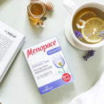 Menopace Night box placed beside a cup of herbal tea with lemon, honey, and flowers on a table.