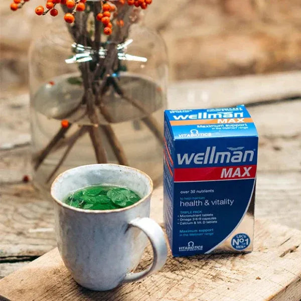 Box of wellman MAX supplement next to a mug with green liquid on a wooden surface.